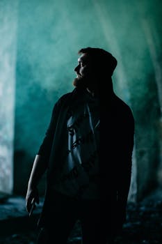 A hooded man looks away in a dark, atmospheric setting, creating a compelling portrait.