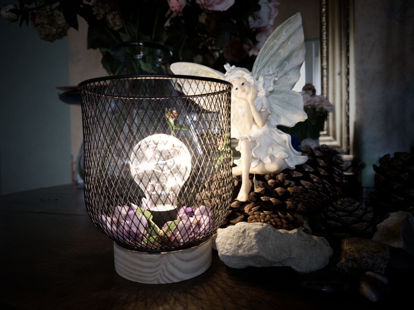 Lampe à ampoule allumée avec des violettes près d'une figurine de fée et de pommes de pin