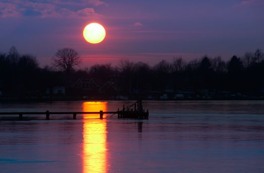 A beautiful sunset over a calm lake with reflections and a silhouetted dock.