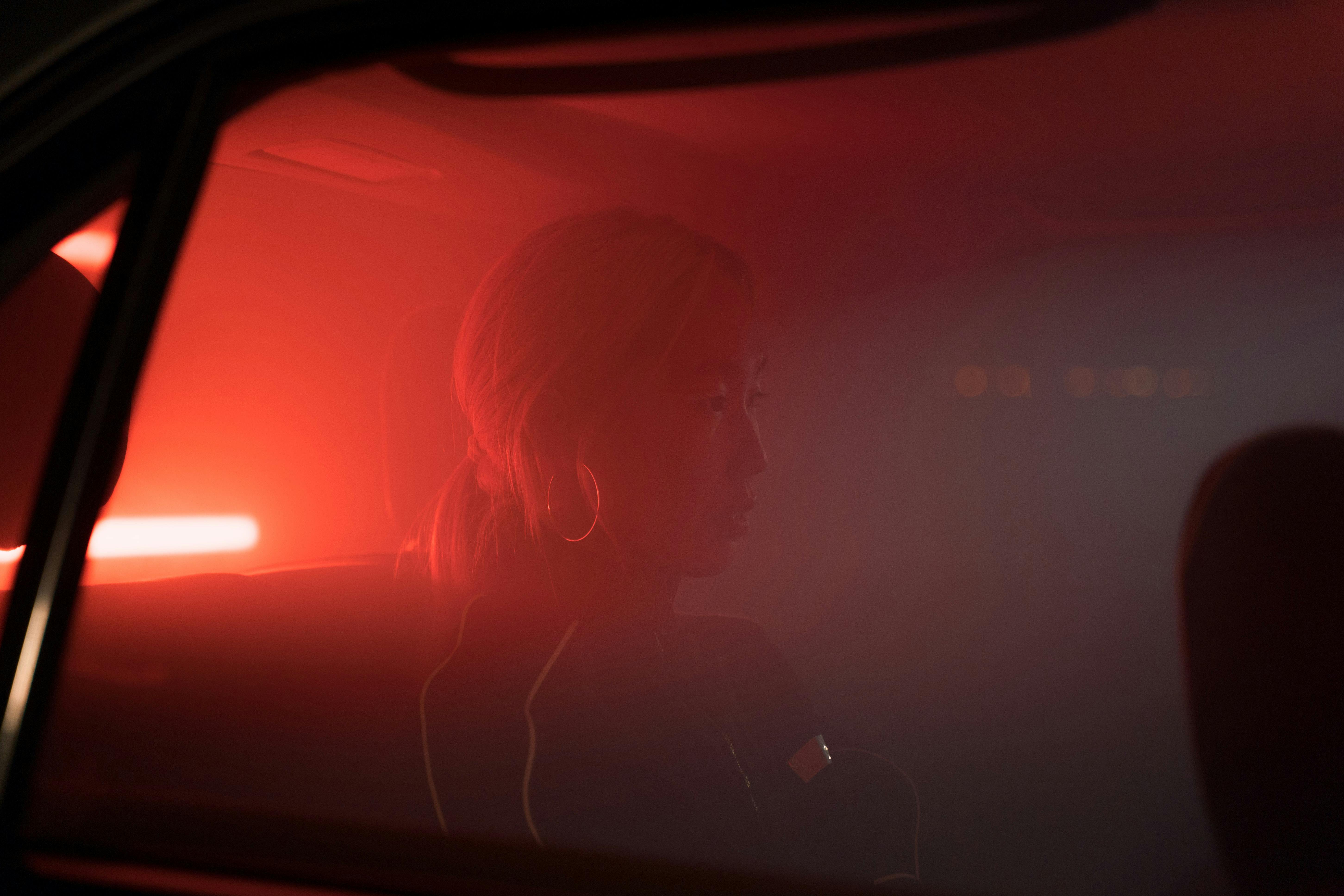 Silhouette of a woman sitting in a smokey car with atmospheric red lighting.