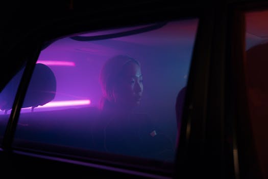 Side view of a woman in a car, illuminated by moody neon pink and purple lights at night.