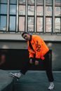 Man in Orange Crew Neck T-shirt and Black Pants Standing on Gray Concrete Floor