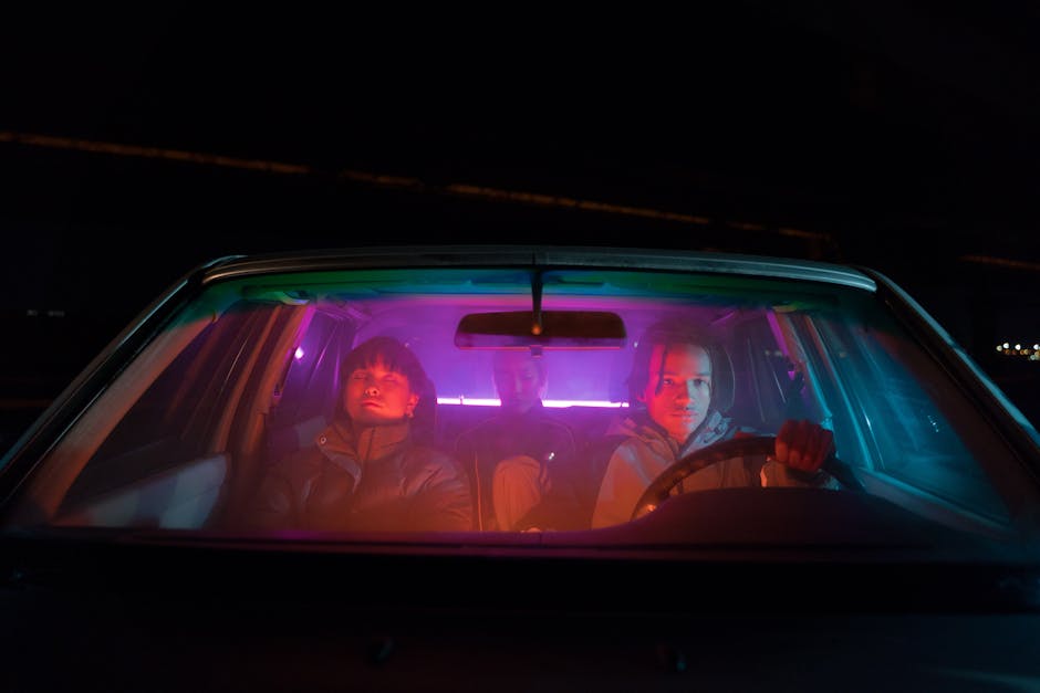 Three adults in a car illuminated by vibrant neon lights, at night.