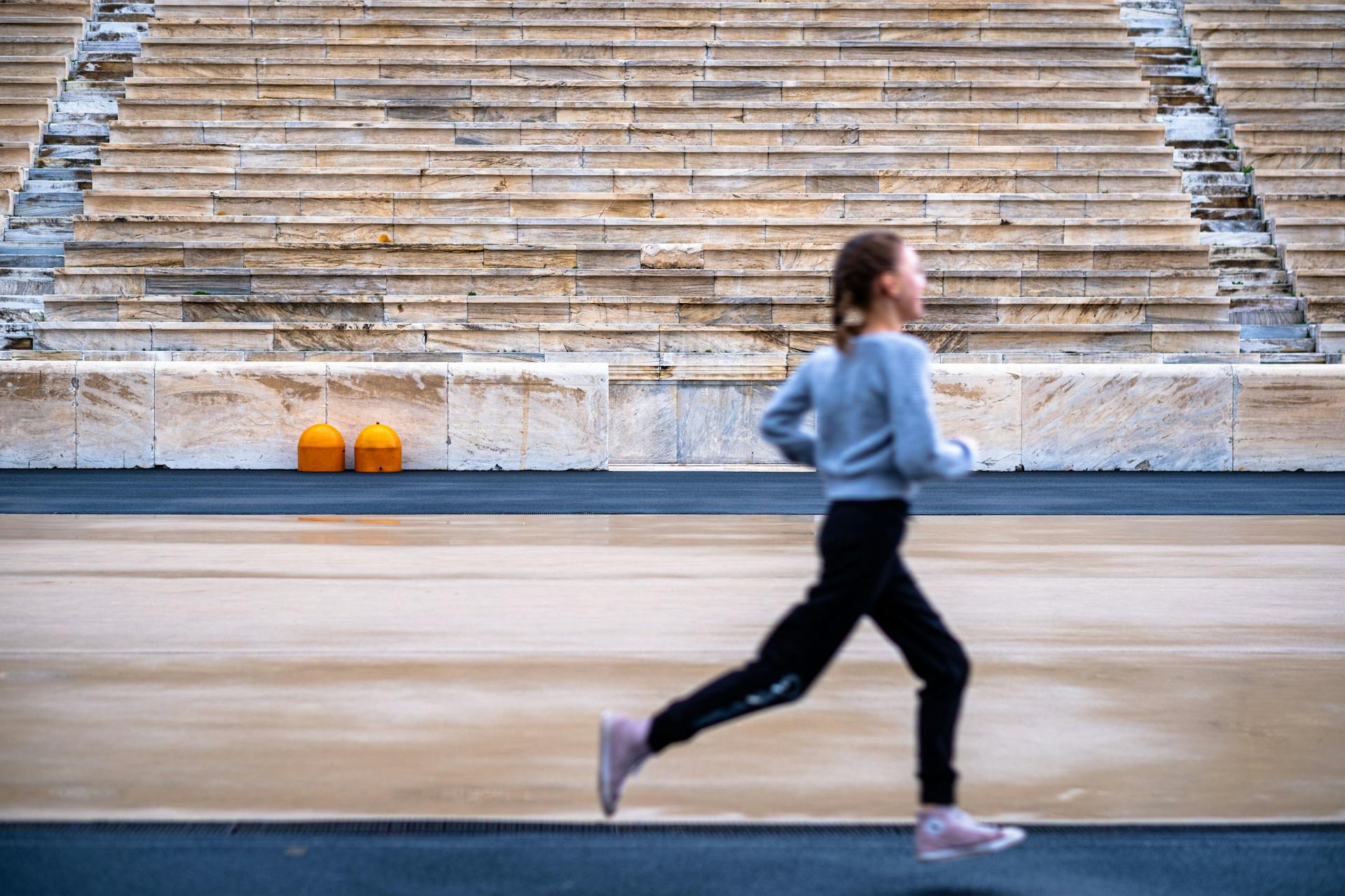 A girl runs in a historic stadium with empty stands, symbolizing youthful energy and ancient architecture.