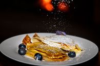 A tempting plate of crepes with blueberries and powdered sugar, perfect for dessert lovers.