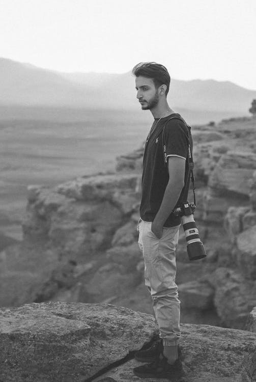 Man in Crew Neck Shirt Standing on Rock with Camera