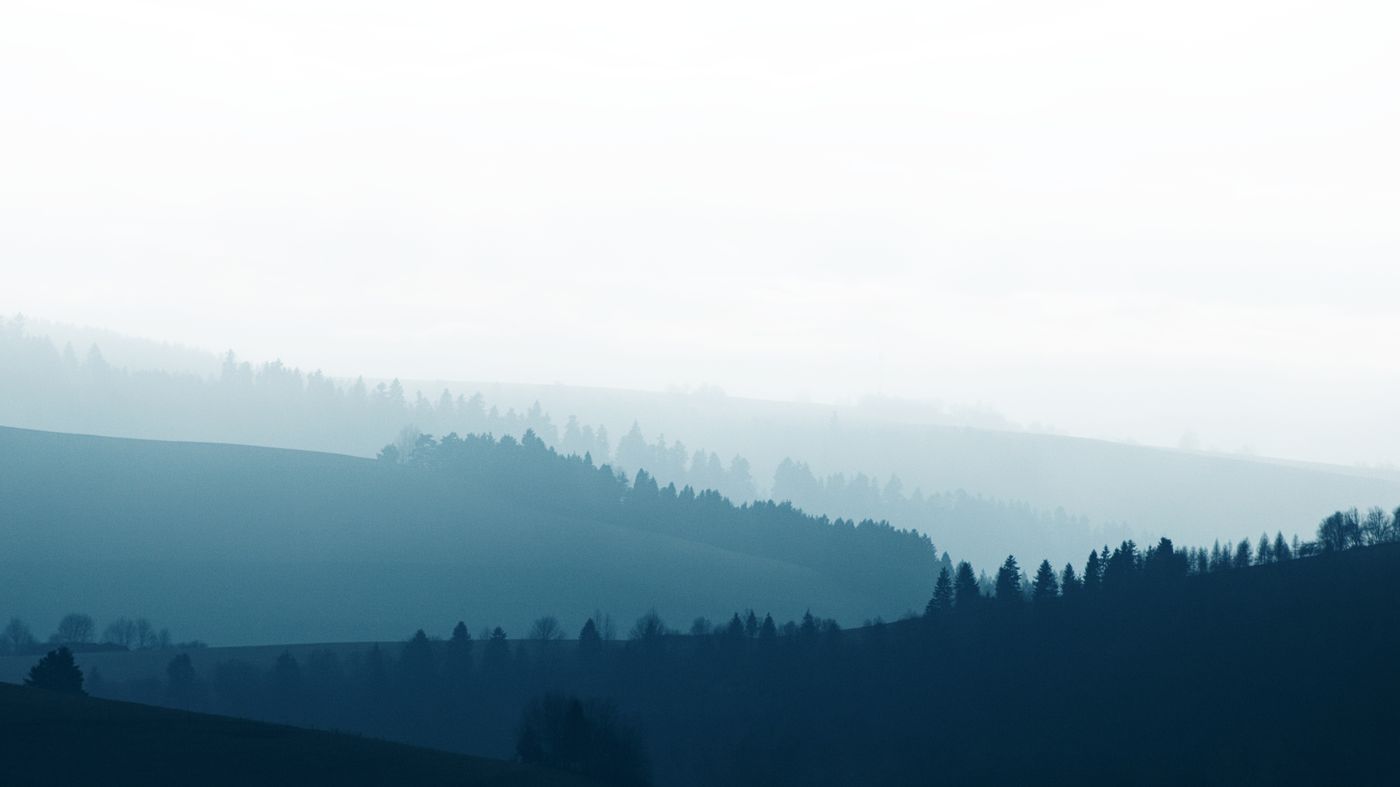 Misty layered hills and forest silhouettes used as a desktop wallpaper — photo by Adrian Regeci on Pexels