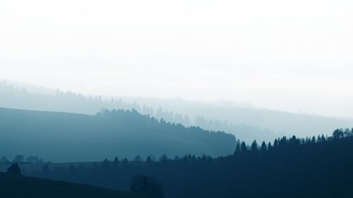 Misty layered hills and forest silhouettes used as a desktop wallpaper — photo by Adrian Regeci on Pexels