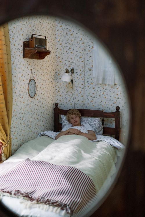 Free Teenage boy with curly hair relaxing in a cozy vintage-style bedroom reflected in a mirror. Stock Photo