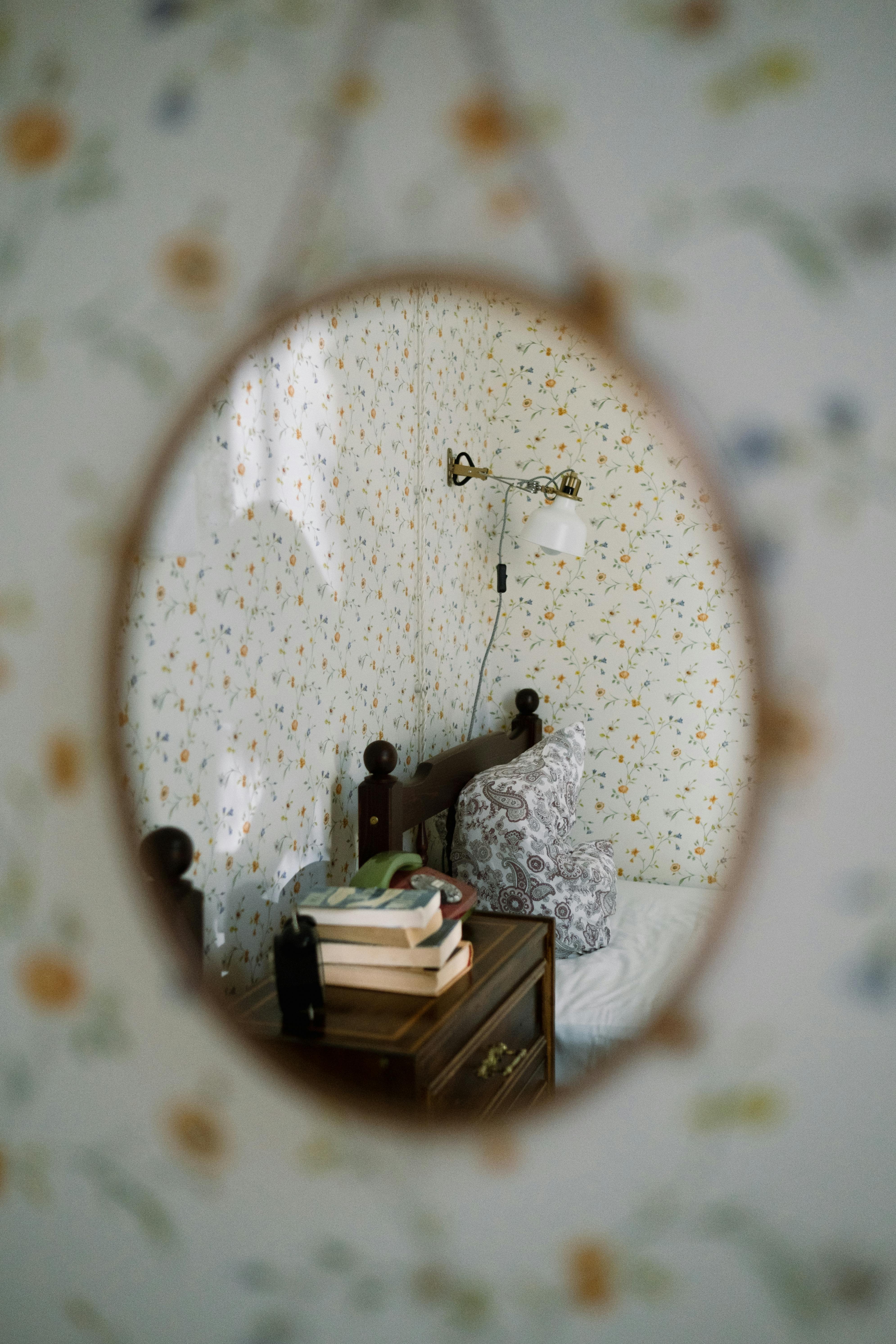 Cozy vintage bedroom with floral wallpaper and books in a mirror reflection.