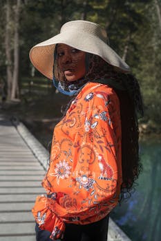 Elegant woman posing in a floral blouse and beige hat on a sunny day outdoors.