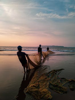Silhouetted fishermen pulling nets along the serene Indian beach during sunrise. Captures the essence of coastal life.