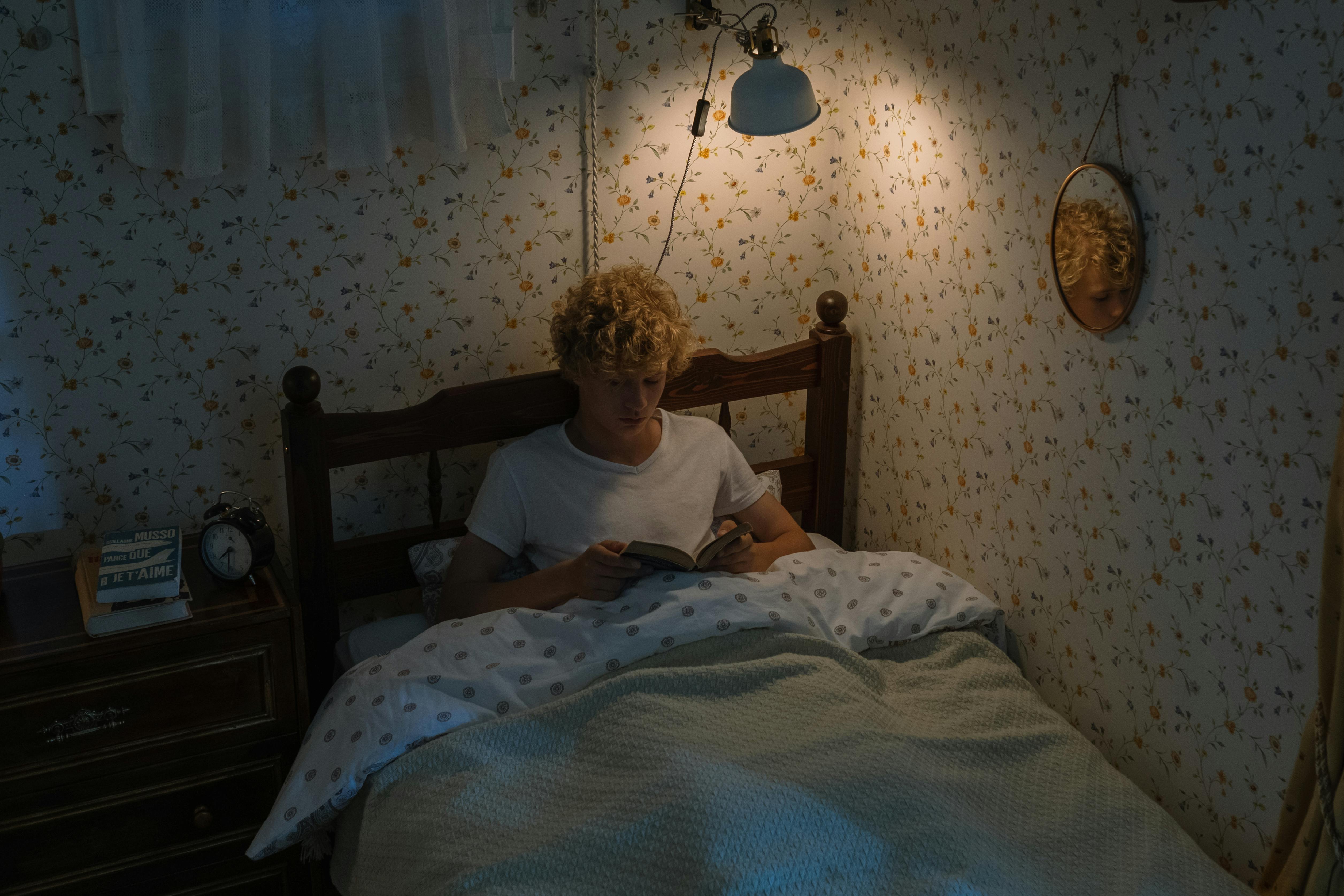 blond teenage boy lying in bed and reading