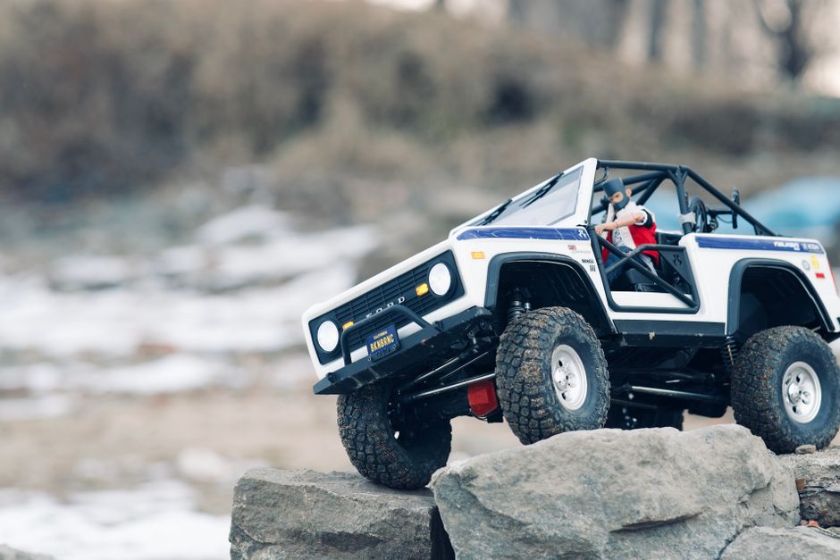 Close-up of a miniature off-road toy car navigating rocky terrain outdoors, showcasing adventure and playfulness.