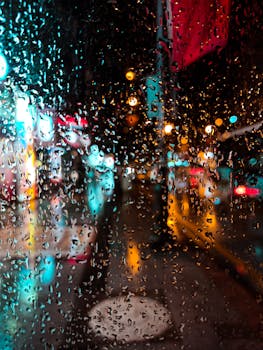 Street city lights reflecting through raindrops on a window at night, creating a colorful bokeh effect.