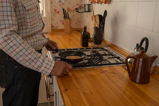 A person cooking pancakes on a gas stove in a cozy country-style kitchen.