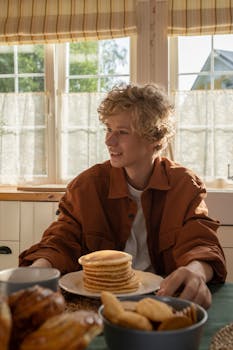 Teenager enjoying a breakfast of pancakes in a brightly lit kitchen setting.