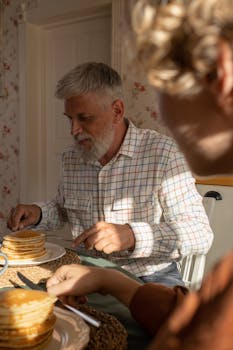A senior man and teenager share a pancake breakfast in a cozy kitchen with morning light.