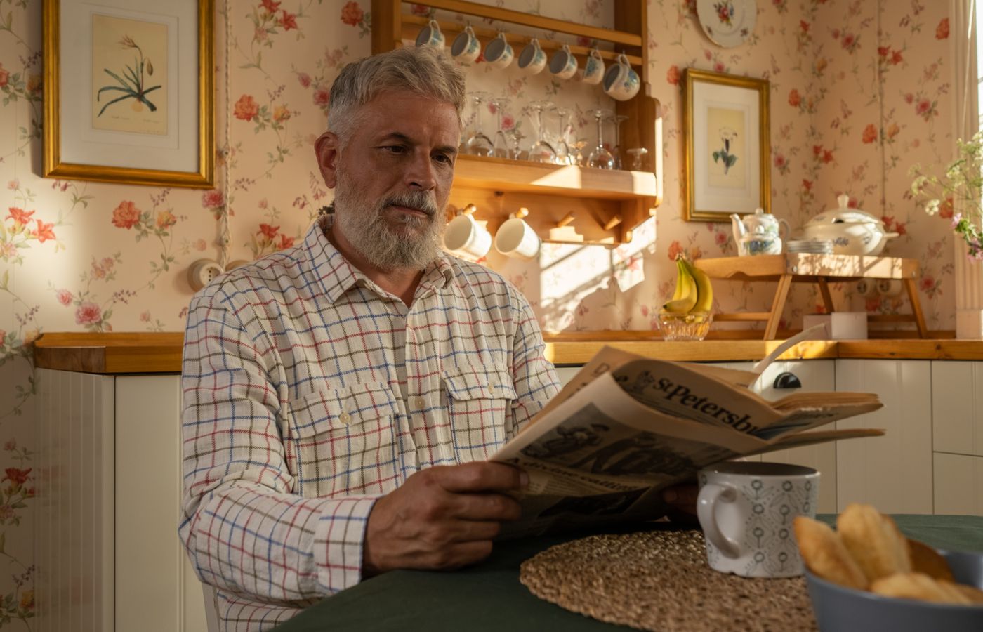 An older man reading the newspaper over breakfast.