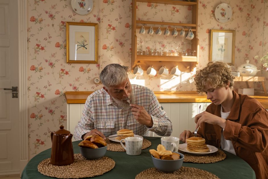Father and son sharing a cozy breakfast of pancakes in a vintage kitchen setting. Father and son sharing a cozy breakfast of pancakes in a vintage kitchen setting.