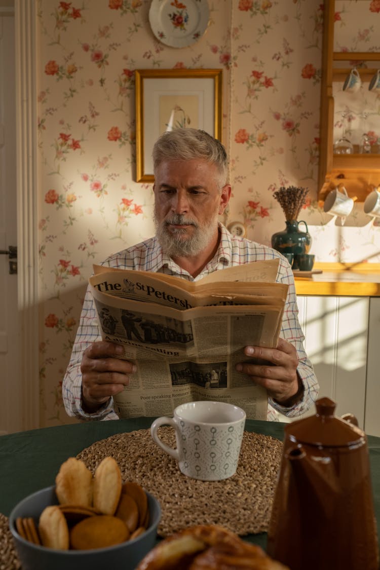 Elderly Man Reading Newspaper In Kitchen