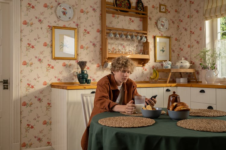 Teenager Sitting In Kitchen And Holding Phone