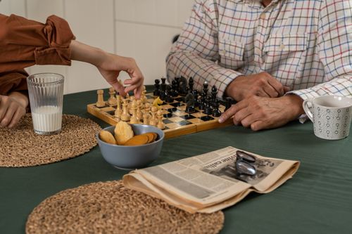 Free Grandfather and teenager enjoying a chess game in the kitchen with milk and cookies. Stock Photo
