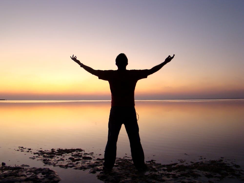 бесплатная Силуэт человека, стоящего на берегу океана во время заката Стоковое фото
