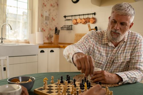 Free Elderly man enjoying a game of chess in a warm, inviting kitchen environment. Stock Photo