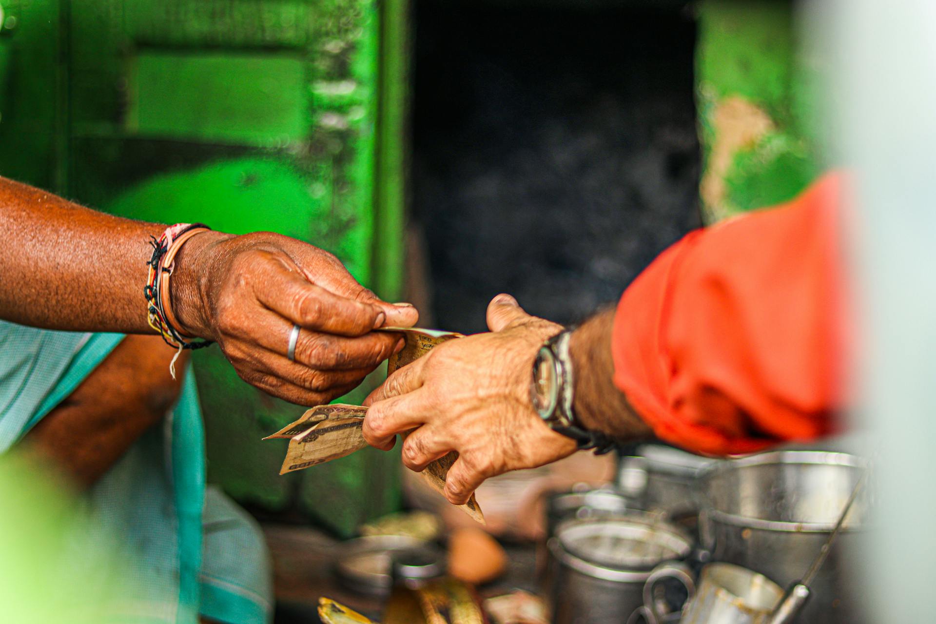 Close view of a transaction where hands exchange paper money, set against a green vendor backdrop.