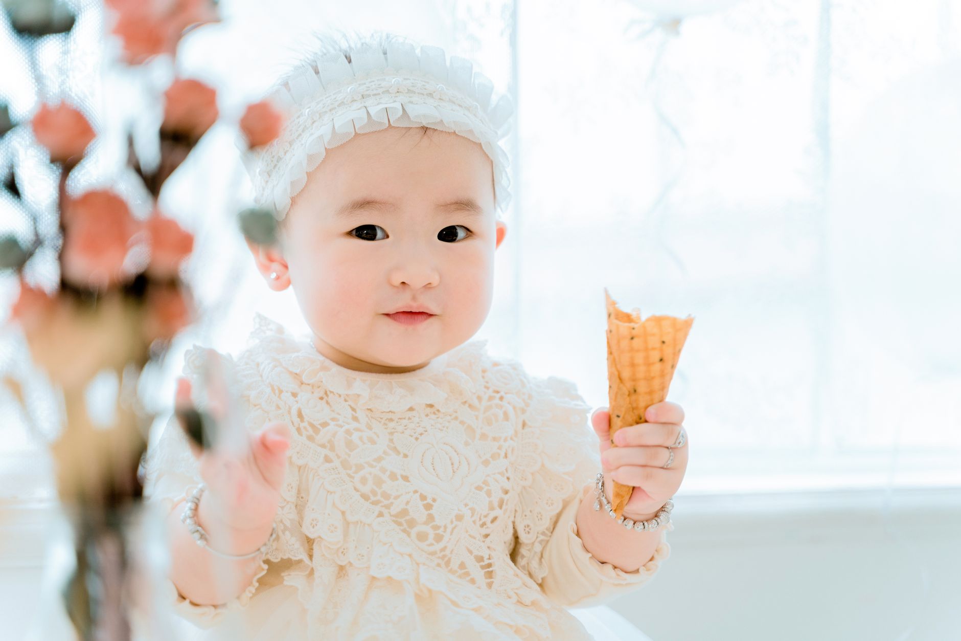 Cute baby holding a waffle cone and smiling in a bright setting.