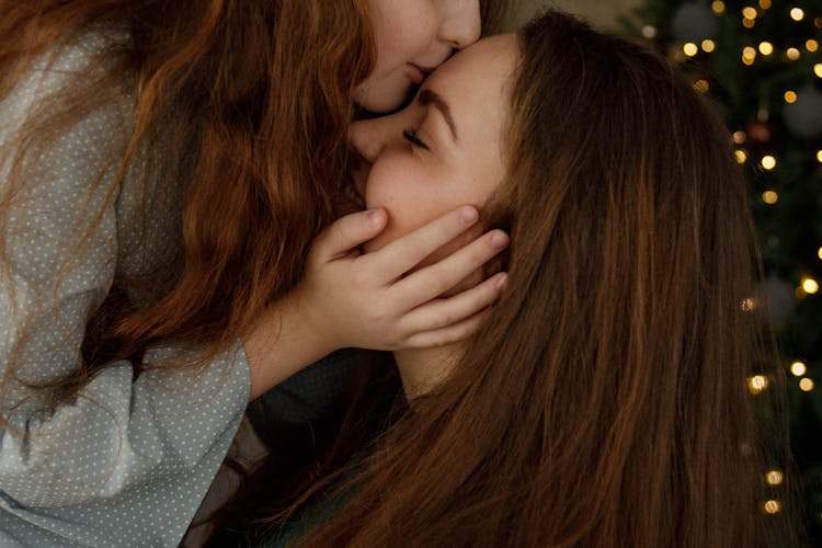 Girl Kissing Her Big Sister In Forehead At Christmas Tree