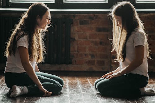 Free Two Teenage Girls Kneeling on Floor Smiling and Looking at Each Other Stock Photo