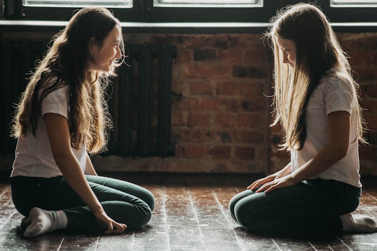 Two Teenage Girls Kneeling On Floor Smiling And Looking At Each Other