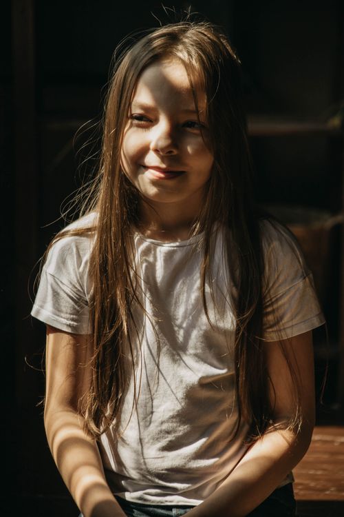Free Close-up portrait of a smiling girl with long hair in a sunlit room, creating a warm and inviting atmosphere. Stock Photo