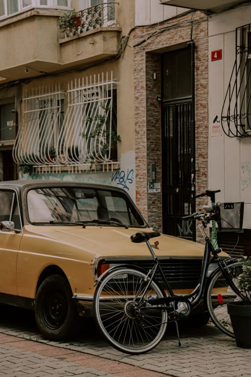 Free Classic yellow car and bicycle parked on a charming city street corner. Stock Photo