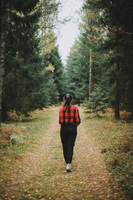 A woman in a red flannel shirt walks down a forest path lined with autumn leaves in Poland.