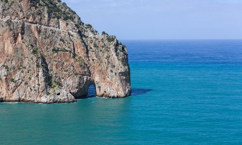 Free Dramatic limestone cliff with a natural arch by the serene blue ocean under a clear sky. Stock Photo