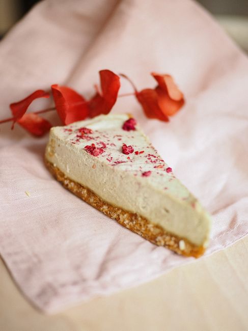 Close-up of a cheesecake slice with red petals on a light napkin, perfect for dessert themes.