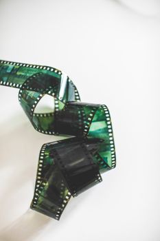 Close-up of tangled green analog filmstrip on a white surface.