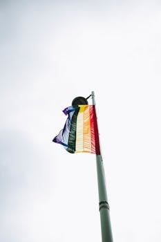 Vibrant LGBTQ pride flag waving high on a pole against a clear sky, representing freedom and diversity.