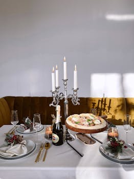 A fine dining setup featuring a candelabra, pizza, and festive tableware on a white tablecloth.