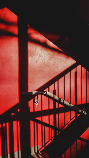 Intriguing shadow play on a vibrant red wall in a stairway, offering a unique aesthetic look.