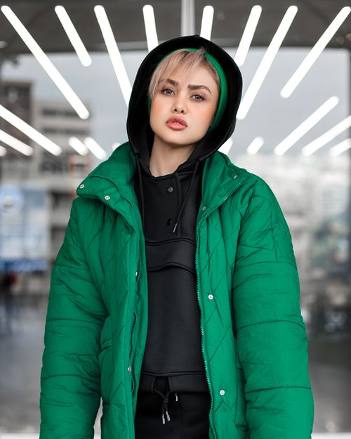 Free Stylish woman in a green jacket poses confidently with urban lights behind her. Stock Photo