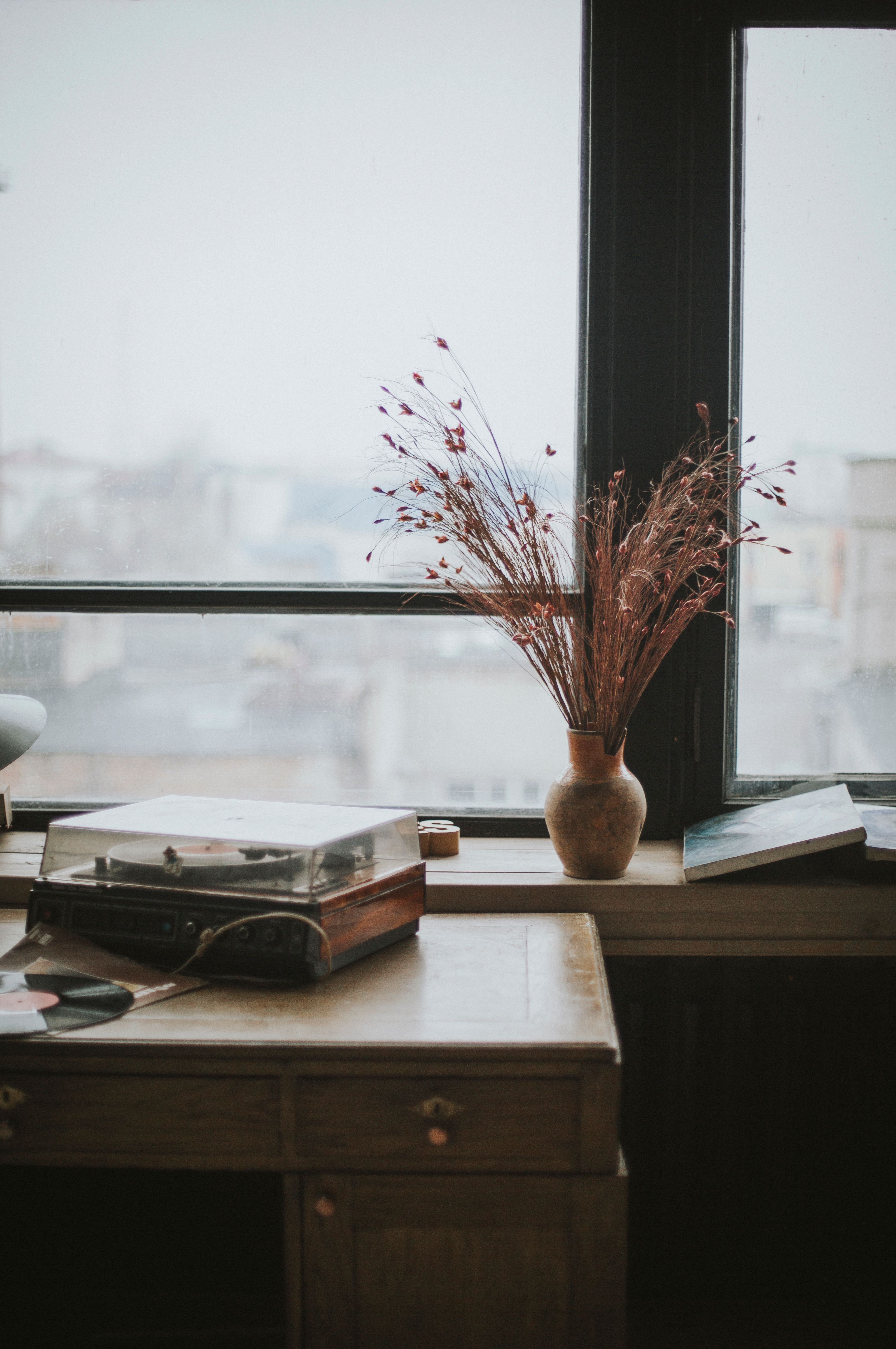 A vintage desk with a vase of dried flowers by a window overlooking an urban skyline.
