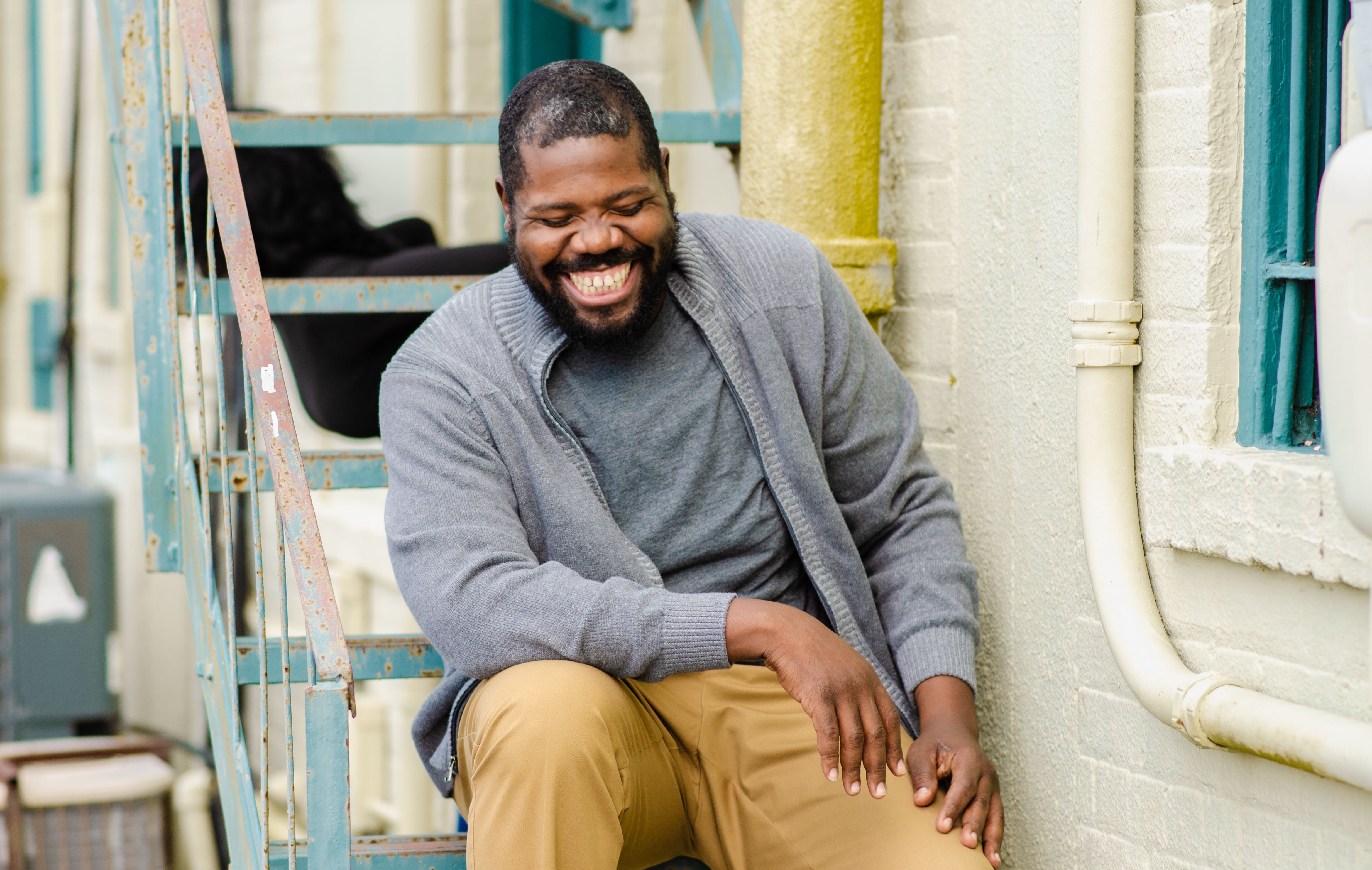 Middle-aged man with a big smile sitting on outdoor fire escape stairs, exuding happiness.