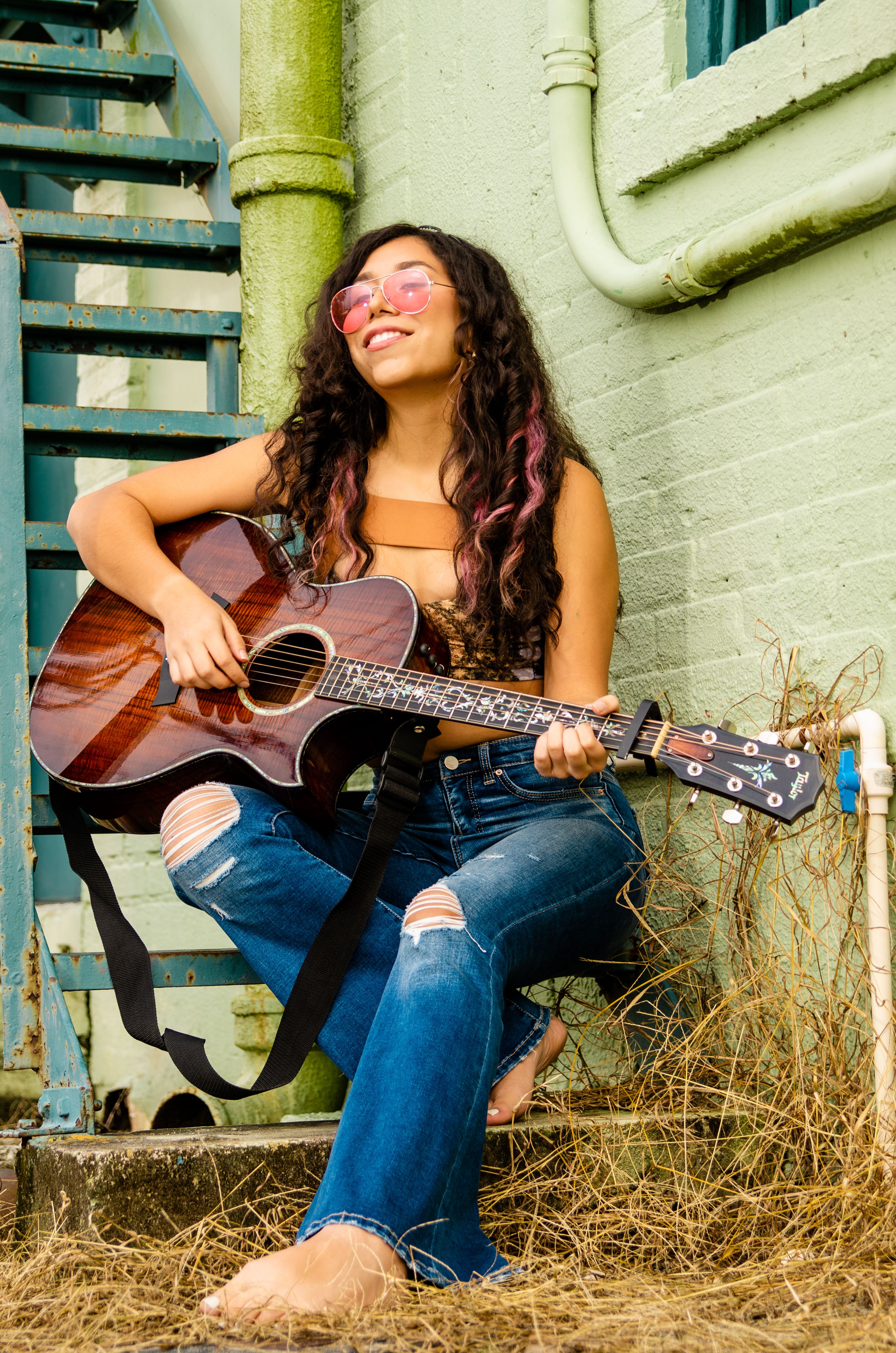Woman playing acoustic guitar while seated outdoors, exuding vibrant, artistic energy.