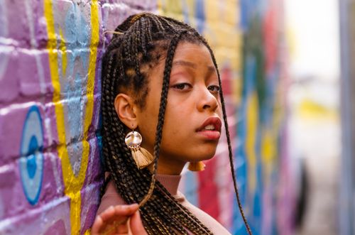 Free Close-up portrait of a woman with braided hair leaning against a colorful graffiti wall. Stock Photo