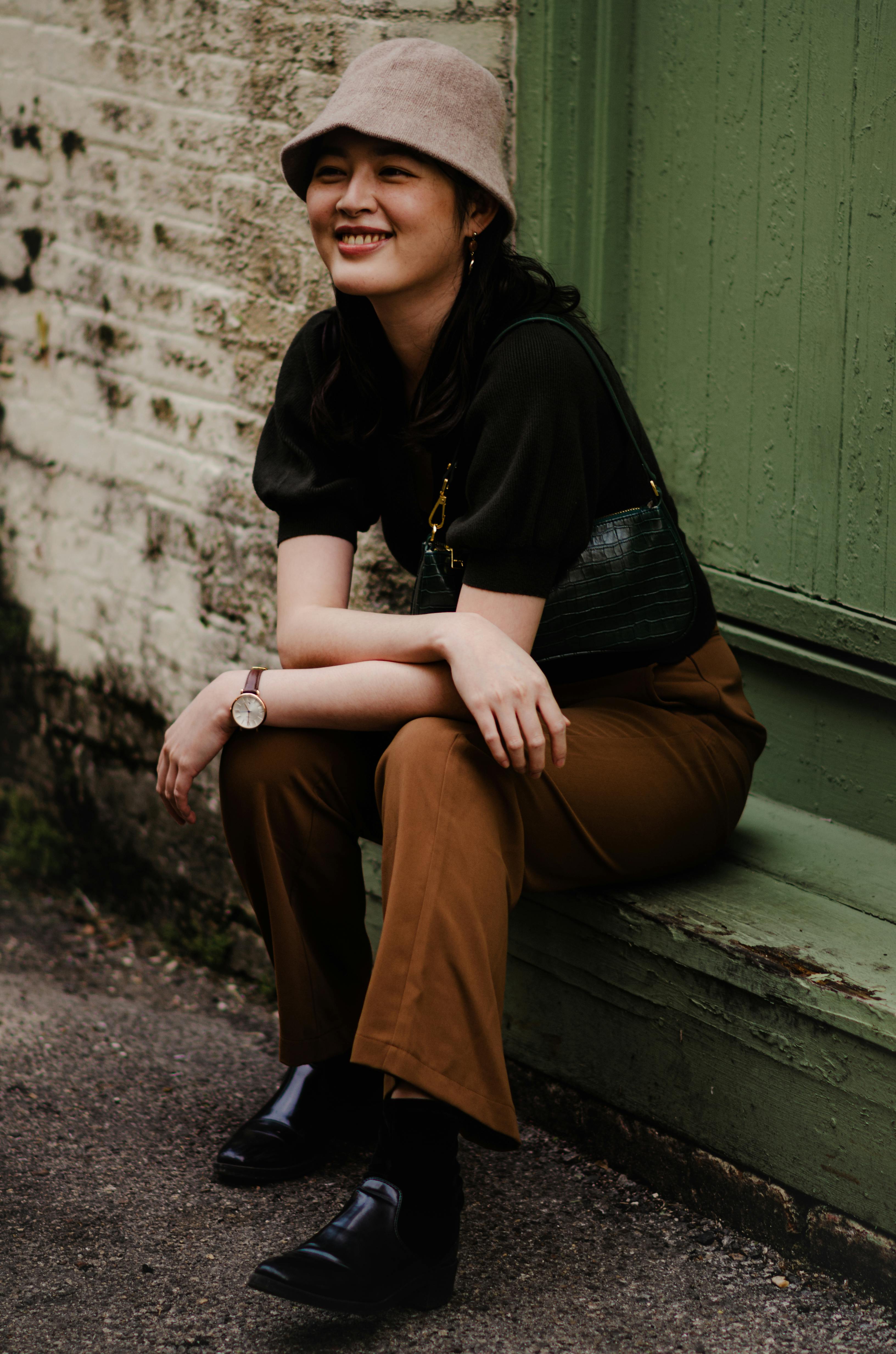 Young woman in casual attire with bucket hat sitting outdoors, smiling.