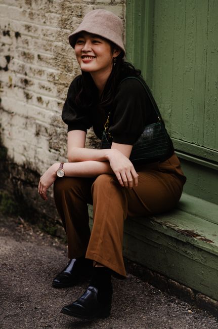 Young woman in casual attire with bucket hat sitting outdoors, smiling.
